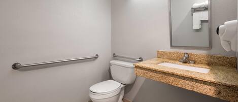 A bathroom with a white toilet, a granite countertop sink, a mirror, and a hand dryer.