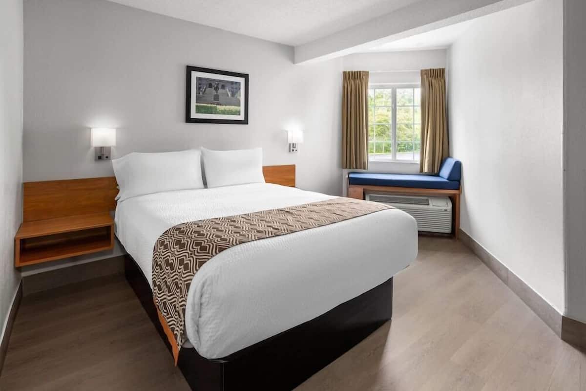 Une chambre d’hôtel comprenant un lit, des lampes de chevet, une fenêtre avec des rideaux et un petit coin salon avec un banc.