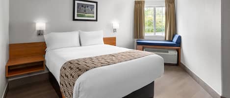 A hotel room with a bed, bedside tables, a window with curtains, and a view of greenery outside.