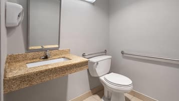 A bathroom with a granite countertop sink, a toilet, a hand dryer, and a handrail.
