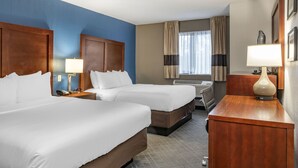 A hotel room with two beds, a desk, a lamp, and a window with curtains. - Comfort Inn University (Buffalo)