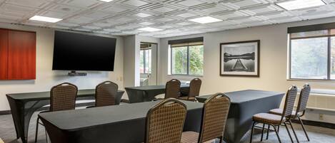 A conference room with a large table, chairs, a flat-screen TV, windows, and a framed picture on the wall.
