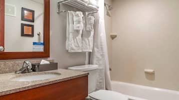 Un baño con lavamanos, inodoro y bañera. Hay toallas colgadas en un perchero y una cortina de ducha.