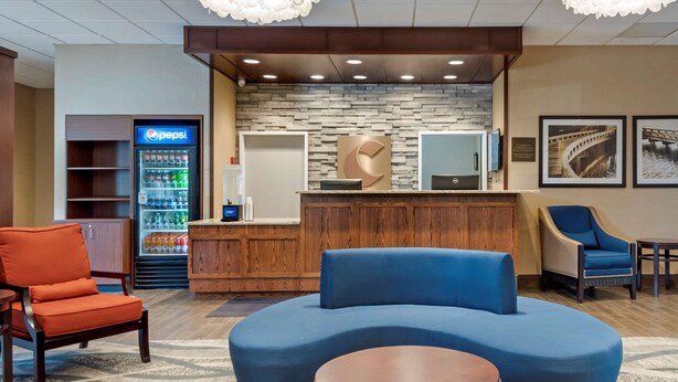 A reception area with a Pepsi refrigerator, a wooden counter, and seating arrangements including a blue sofa and orange chairs. - Comfort Inn University (Buffalo)