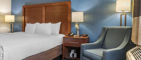 A hotel room with a wooden headboard, a bed with white linens, two bedside tables with lamps, a blue armchair, and a heater.