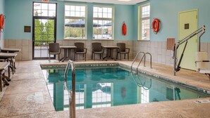A swimming pool area with a tiled floor, a pool with a safety ladder, and several chairs and tables. - Comfort Inn University (Buffalo)