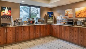 A breakfast bar with a wooden finish, a fruit juice dispenser, a microwave, and a refrigerated display case. - Comfort Inn University (Buffalo)