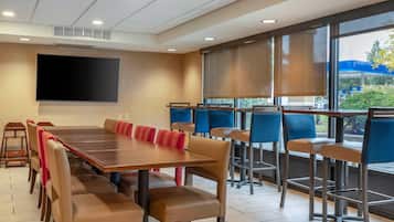 A conference room with a long table, multiple chairs, a large screen, and large windows with blinds.