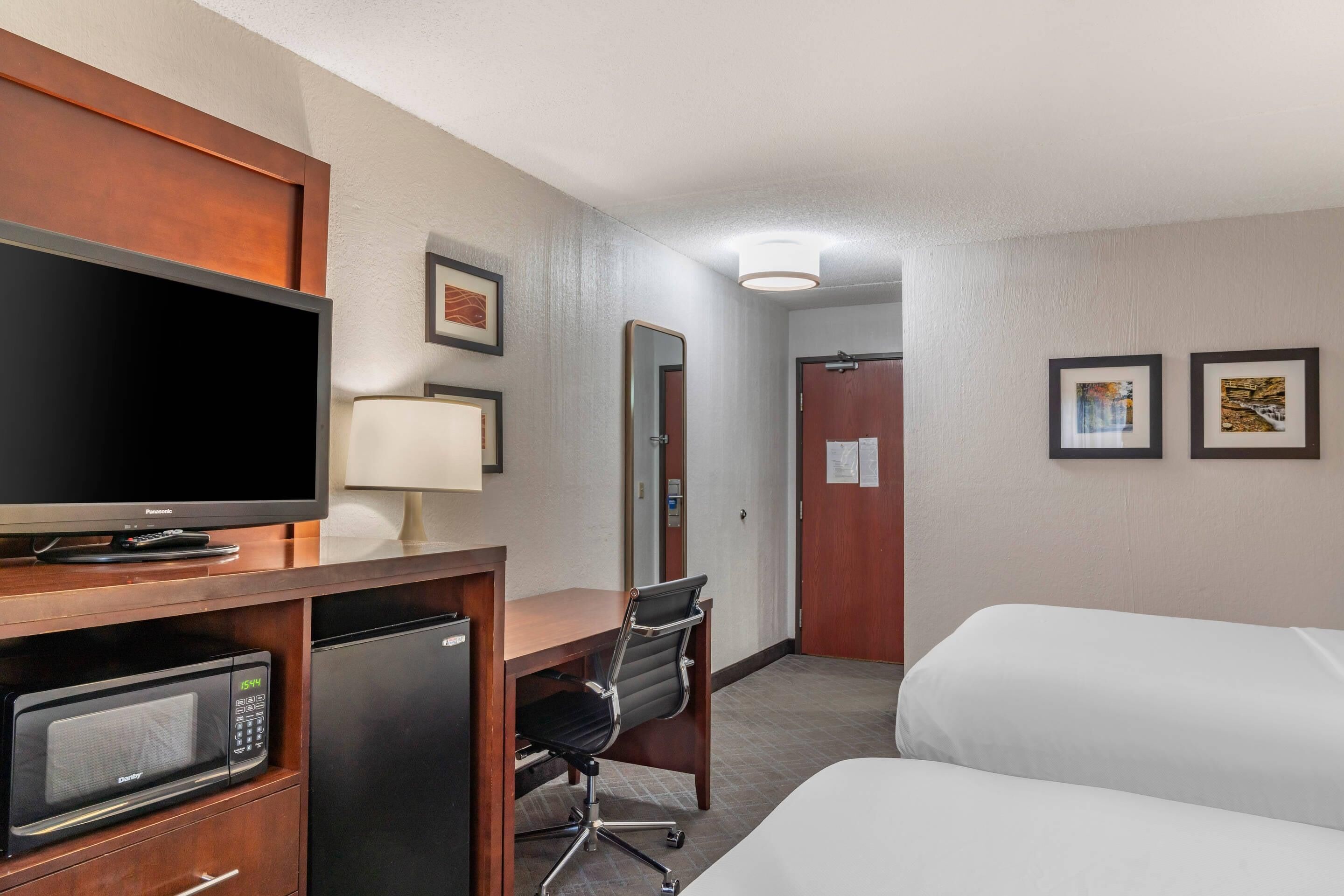 A hotel room with a bed, a desk with a computer, a microwave, and a television.