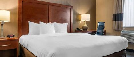 A hotel room with a large bed, two bedside tables, a desk, a chair, and a window with curtains.