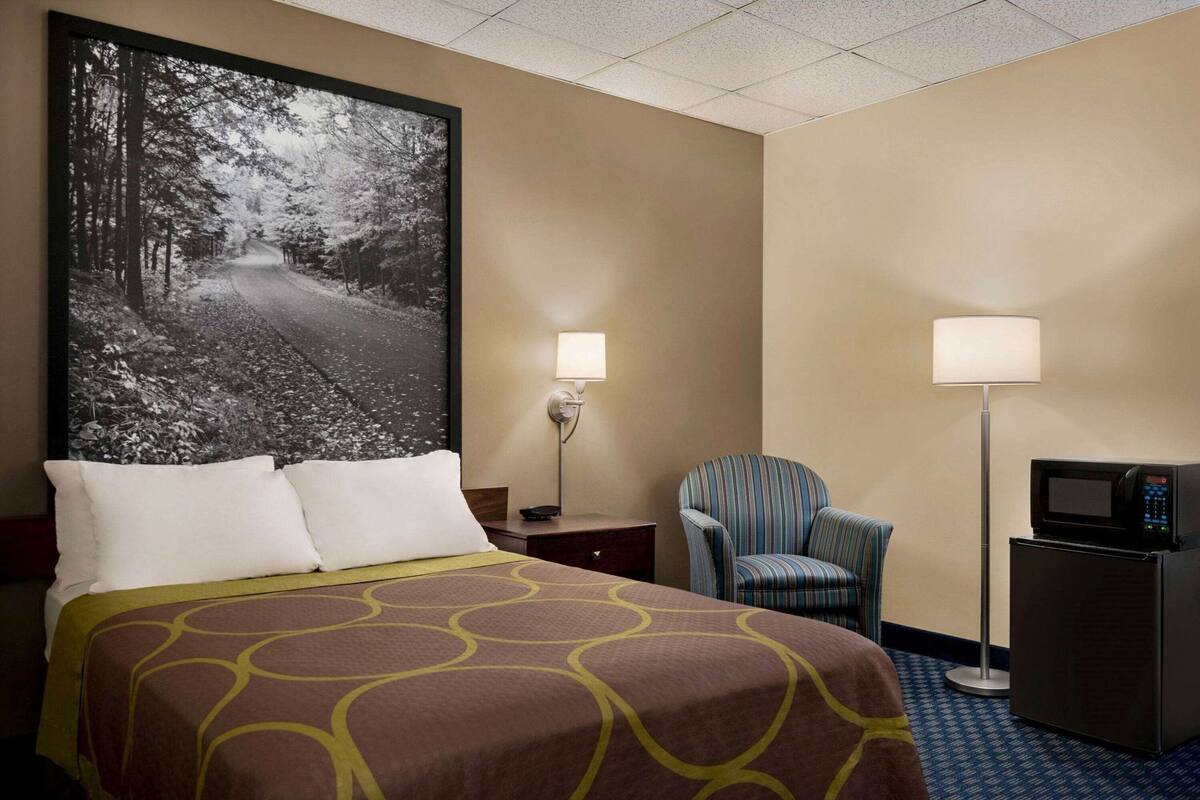 A hotel room with a large bed, a chair, a desk with a lamp, and a microwave.