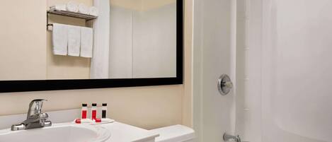 Un baño con lavamanos, inodoro y bañera. Hay un espejo sobre el lavamanos, y se ven toallas al fondo.