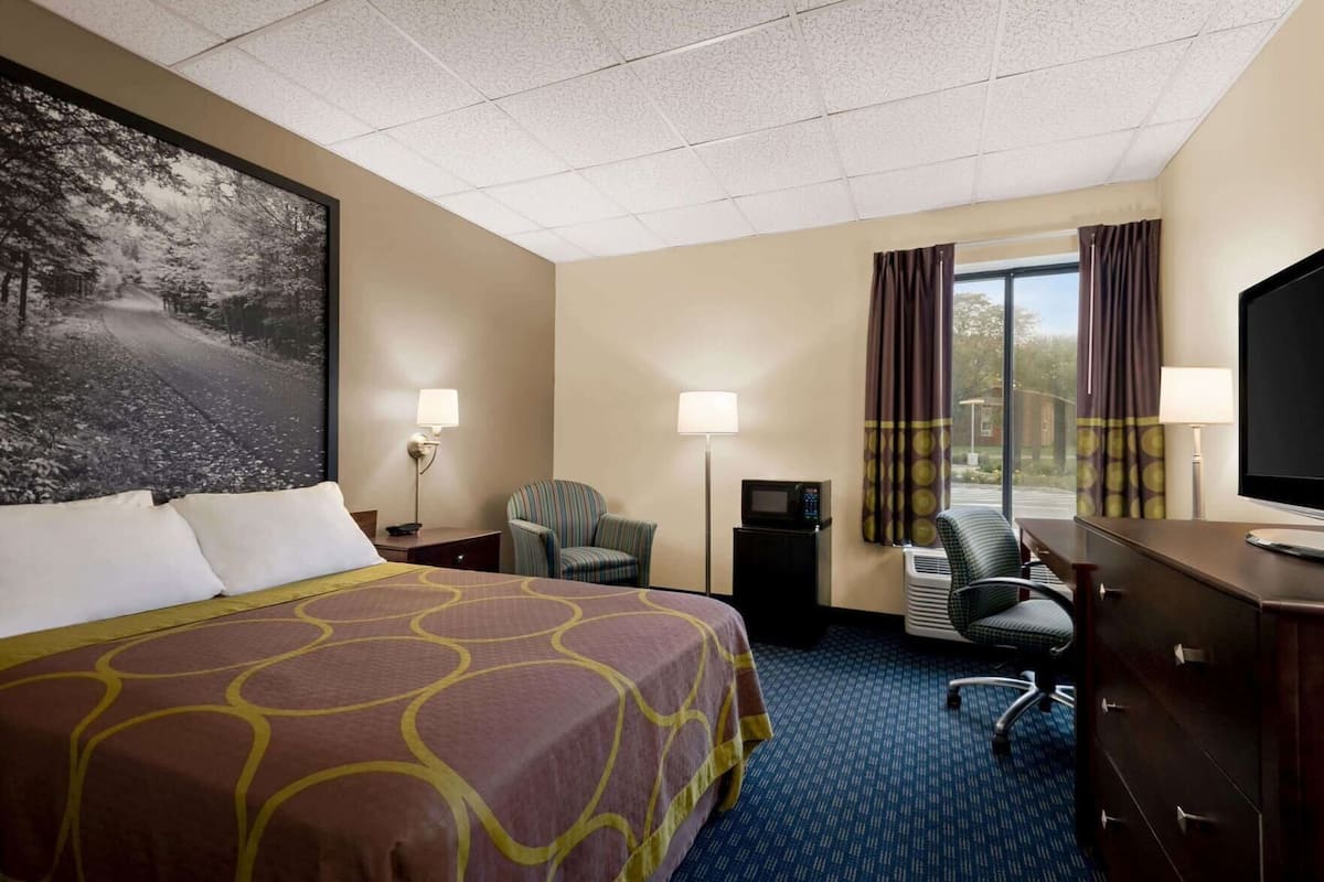 A hotel room with a large bed, a desk with a chair, a television, a lamp, and a window with curtains.