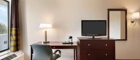 A hotel room with a desk, chair, television, dresser, and a bed.
