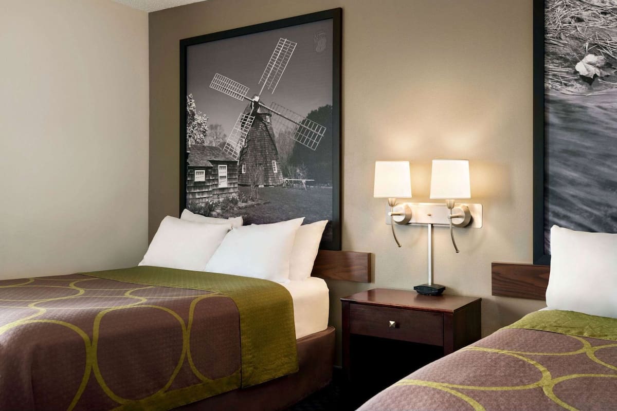 A hotel room with two beds, a nightstand with lamps, a framed picture of a windmill, and a wall-mounted artwork.