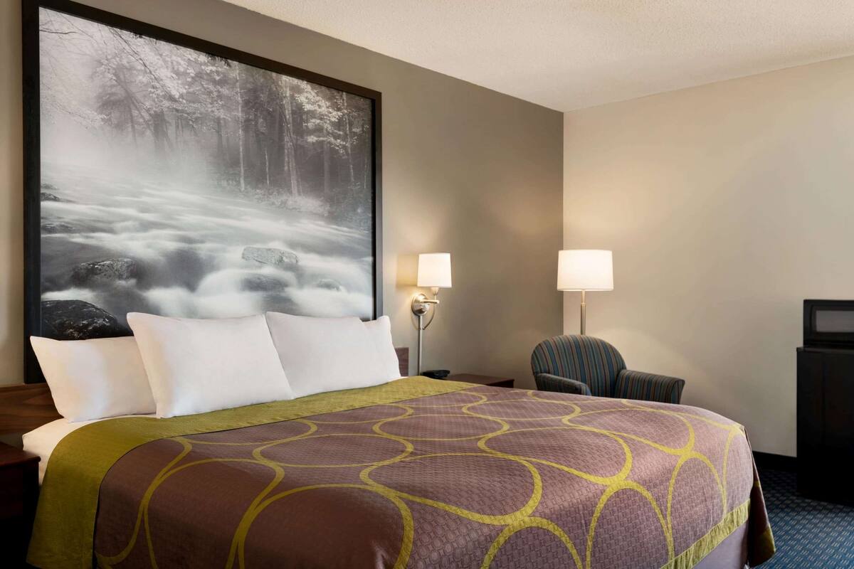 A hotel room with a large bed, two bedside lamps, a chair, and a television on a cabinet.