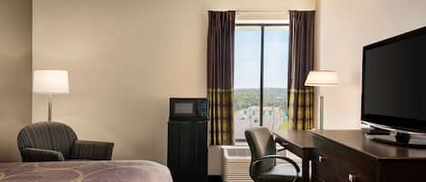 A hotel room with a bed, a desk with a television, a chair, a desk lamp, and a view of the city through the window.