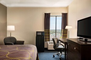 Ein Hotelzimmer mit Bett, Schreibtisch mit Fernseher, Stuhl, Schreibtischlampe und Blick auf die Stadt durch das Fenster.