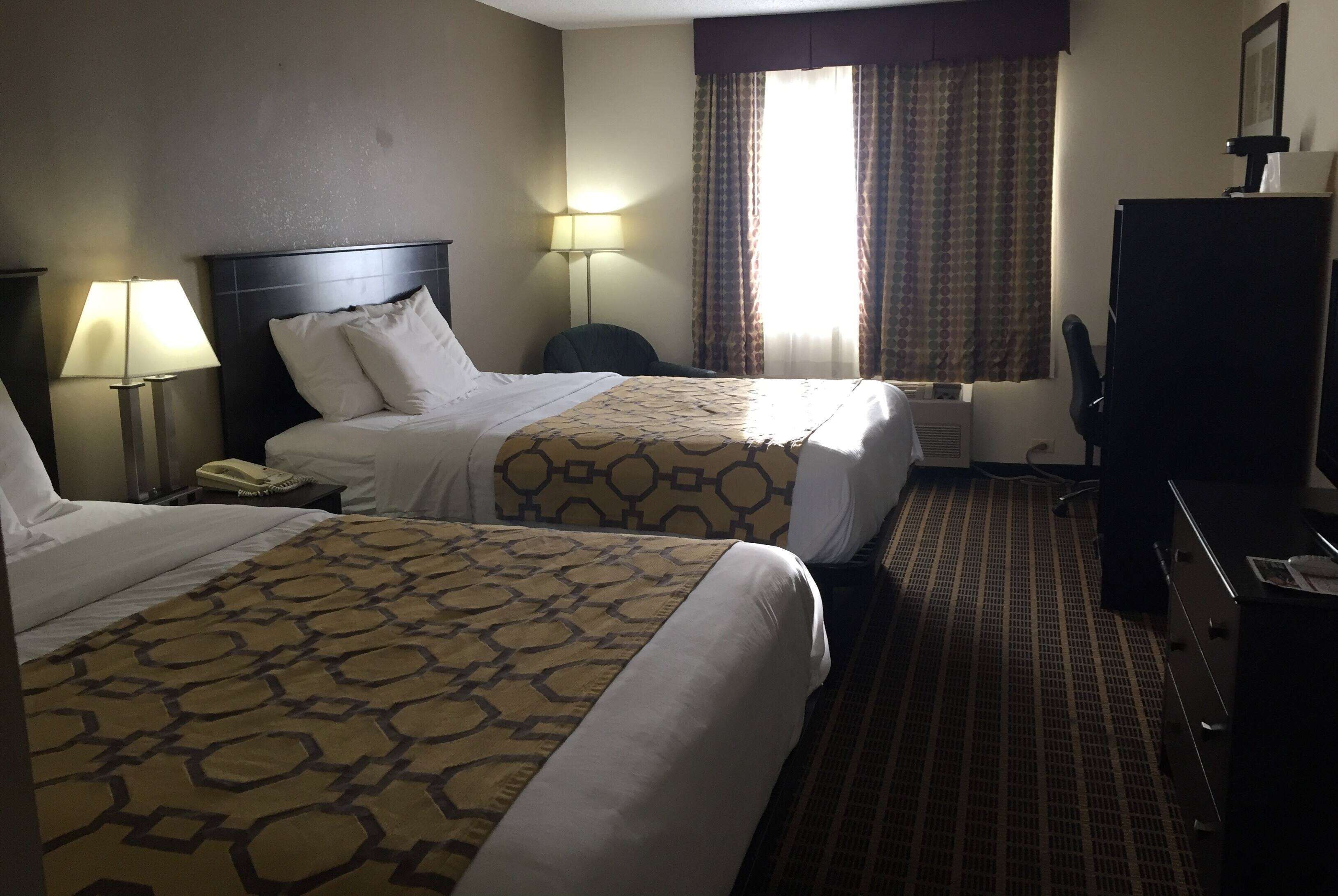 A hotel room with two beds, a desk, a chair, a lamp, and a window with curtains.