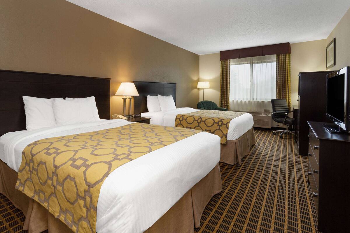 Een hotelkamer met twee bedden, elk voorzien van een bedsprei met dessin, een bureau met stoel, een televisie en een raam met gordijnen.