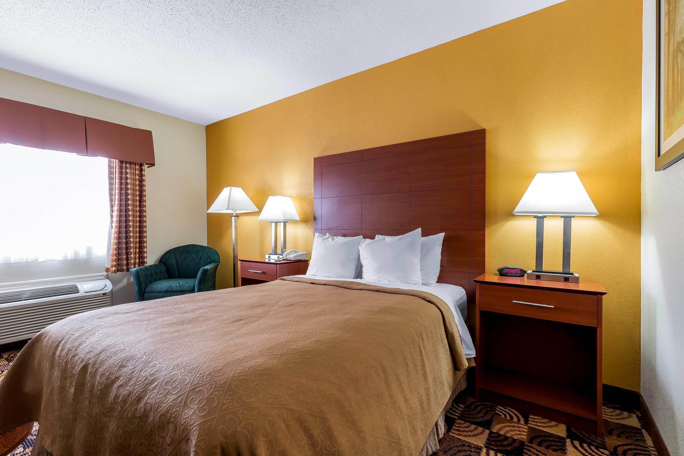 A hotel room with a large bed, two bedside tables with lamps, a chair, and a window with curtains.
