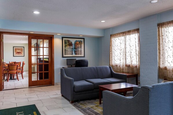 A living room with a sofa, a coffee table, and a television. There is a door leading to a dining area with chairs and a table.