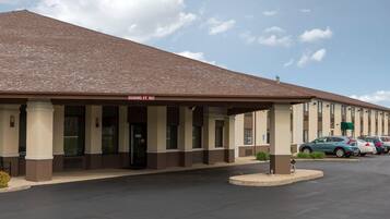 A motel with a covered entrance, a clear sky, and a parking lot with cars.