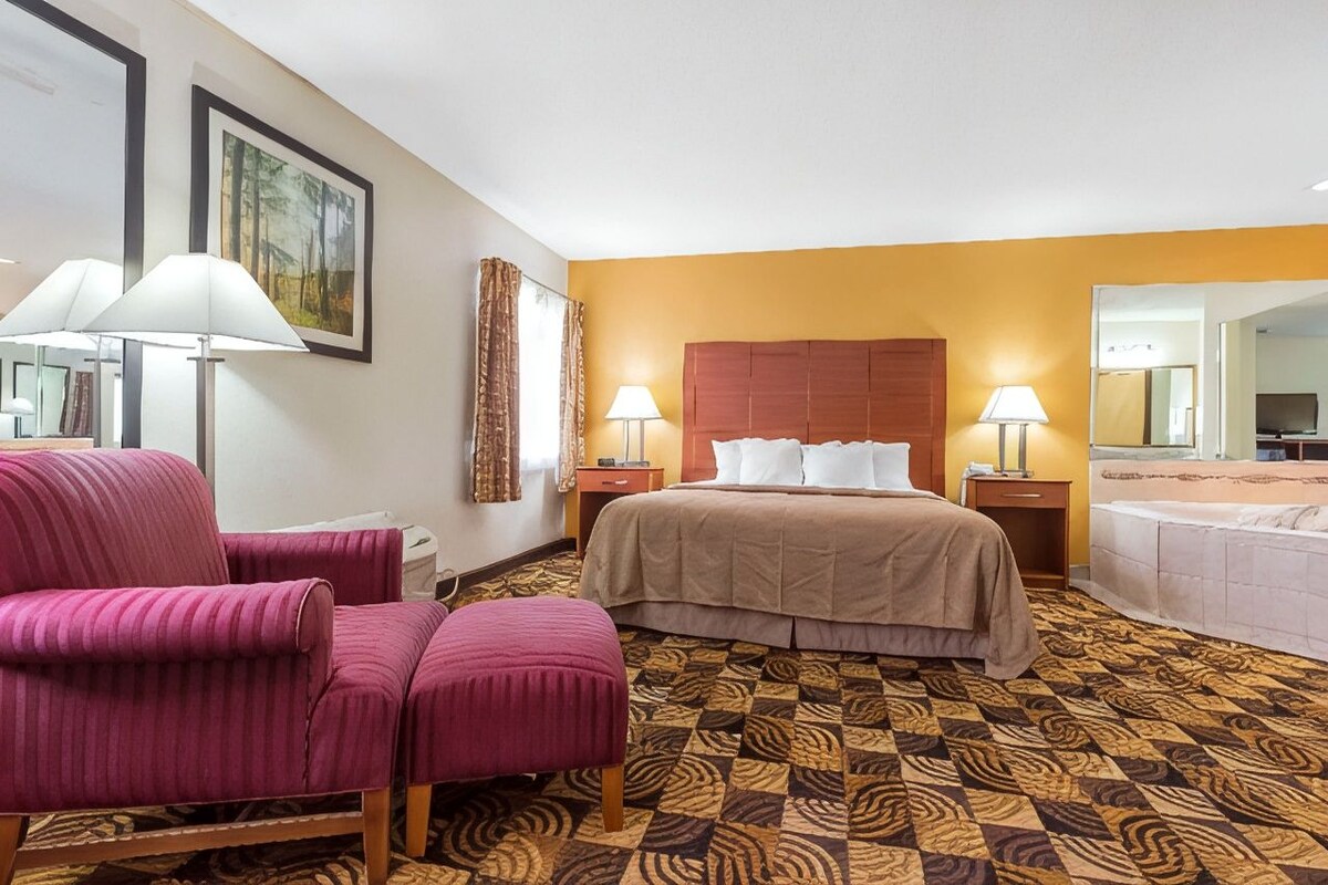A hotel room with a bed, two bedside lamps, a chair, a small table, and a mirror.
