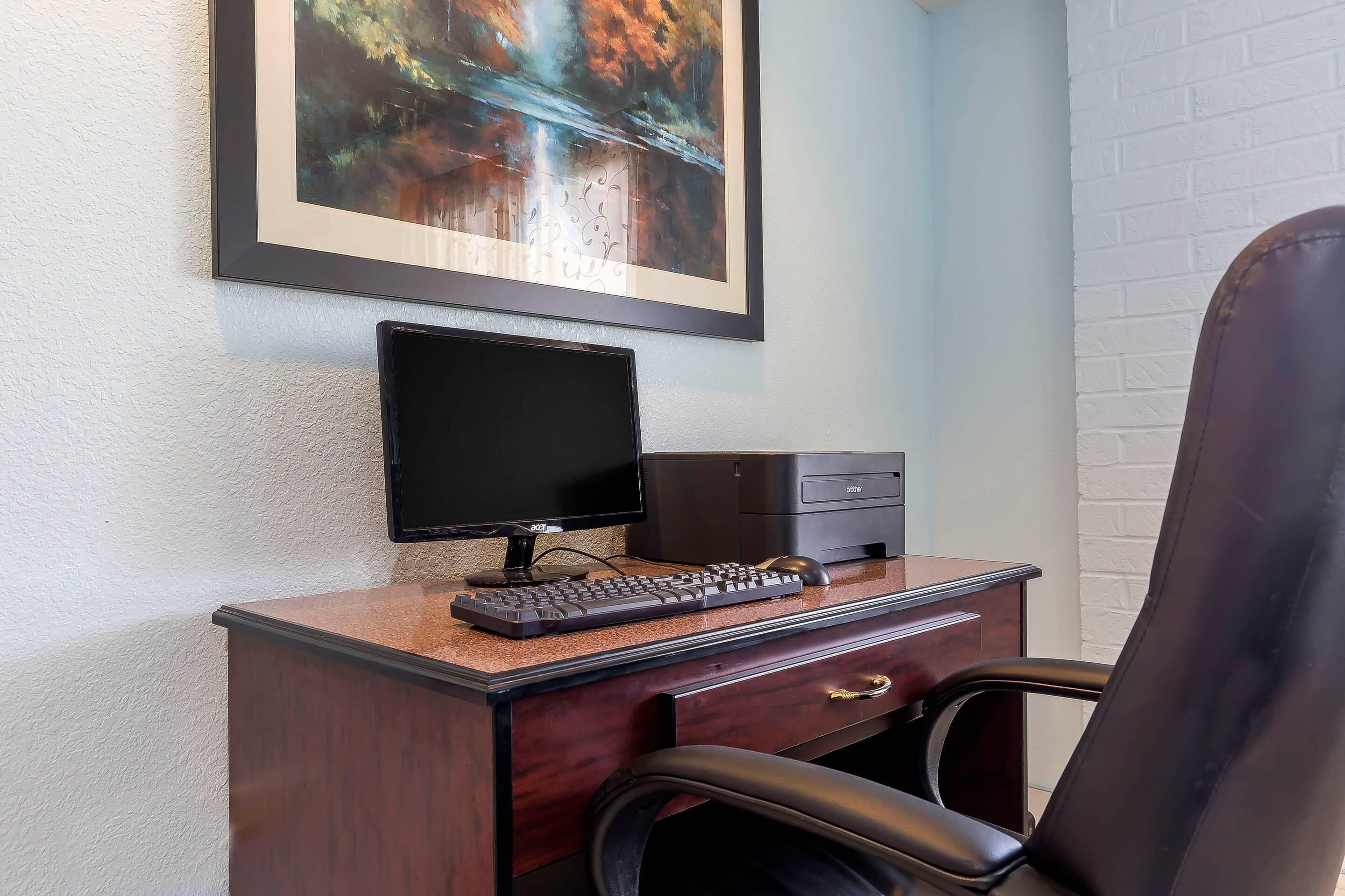 A desk with a computer, keyboard, and mouse, a chair, and a framed painting on the wall.