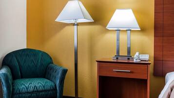 A hotel room with a teal armchair, a wooden nightstand with a phone, and two floor lamps.