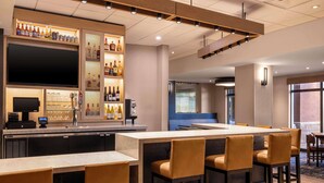 A bar area with a long counter, multiple seating options, and a variety of bottles and glasses. - Hyatt Place Tempe Phoenix Airport (Tempe)