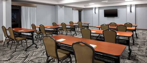 A conference room with multiple tables and chairs, a flat-screen TV on the wall, and a patterned carpet.