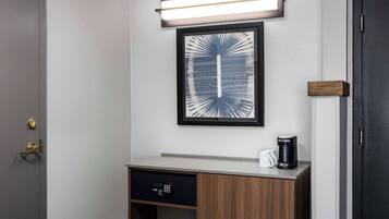 Habitación de hotel con una obra de arte enmarcada, una cafetera y un panel de control sobre un mueble de madera.