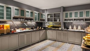 A modern kitchen with grey cabinets, a herringbone tile backsplash, and a central island with a glass top. - Hyatt Place Tempe Phoenix Airport (Tempe)