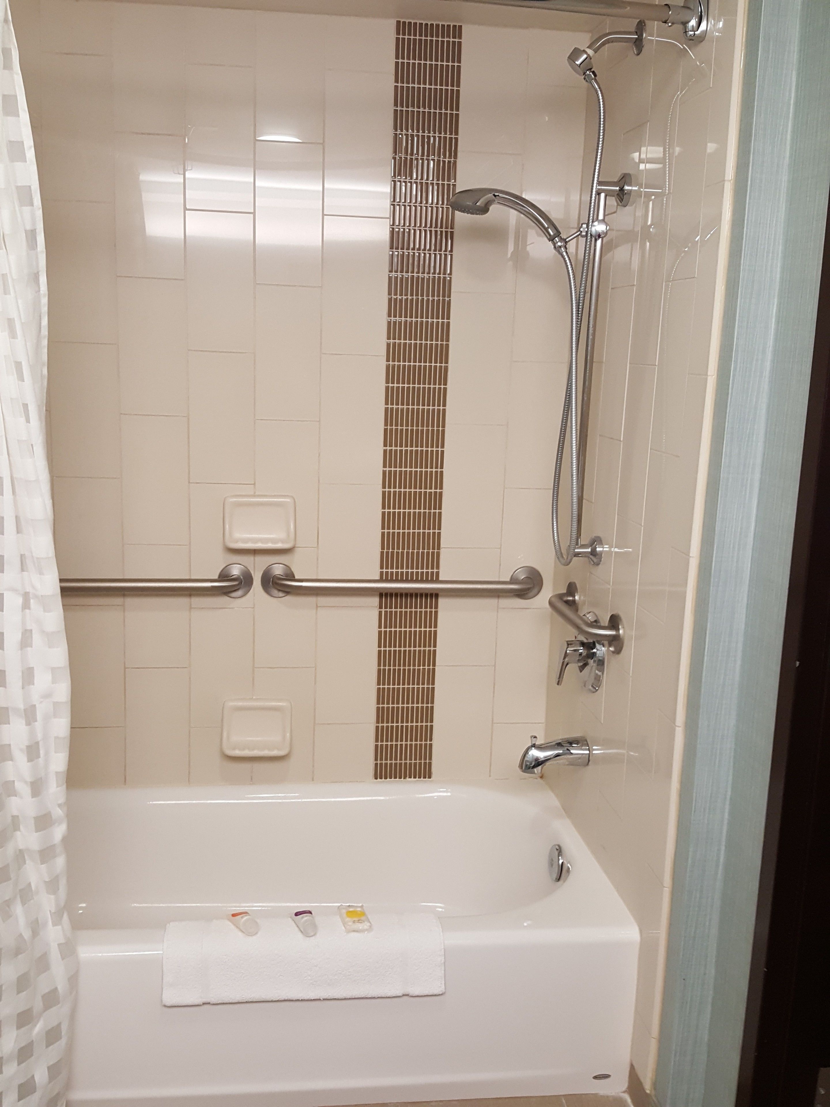 A bathroom with a bathtub, a shower, and a handrail.