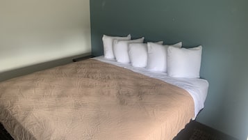 Un lit bien fait, recouvert d’une couvre-lit beige et agrémenté d’oreillers blancs, dans une pièce aux murs de couleur turquoise.