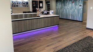 A reception area with a wooden reception desk, a computer, and a clock. There are exit signs on the wall and a patterned wall behind the desk. - Baymont by Wyndham Boardman (Boardman)