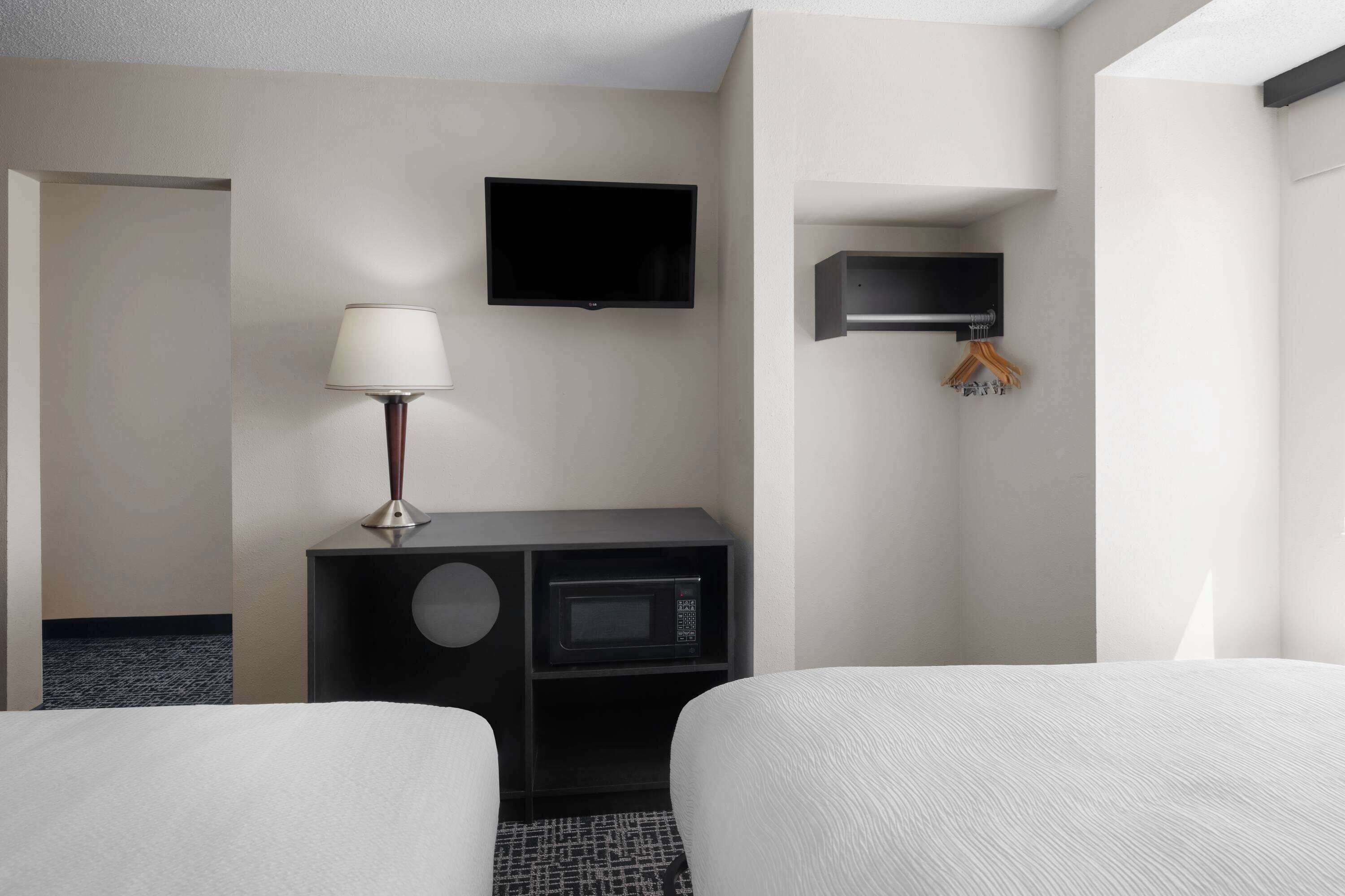 A hotel room with two beds, a flat-screen TV, a lamp, a microwave, and a coat rack.