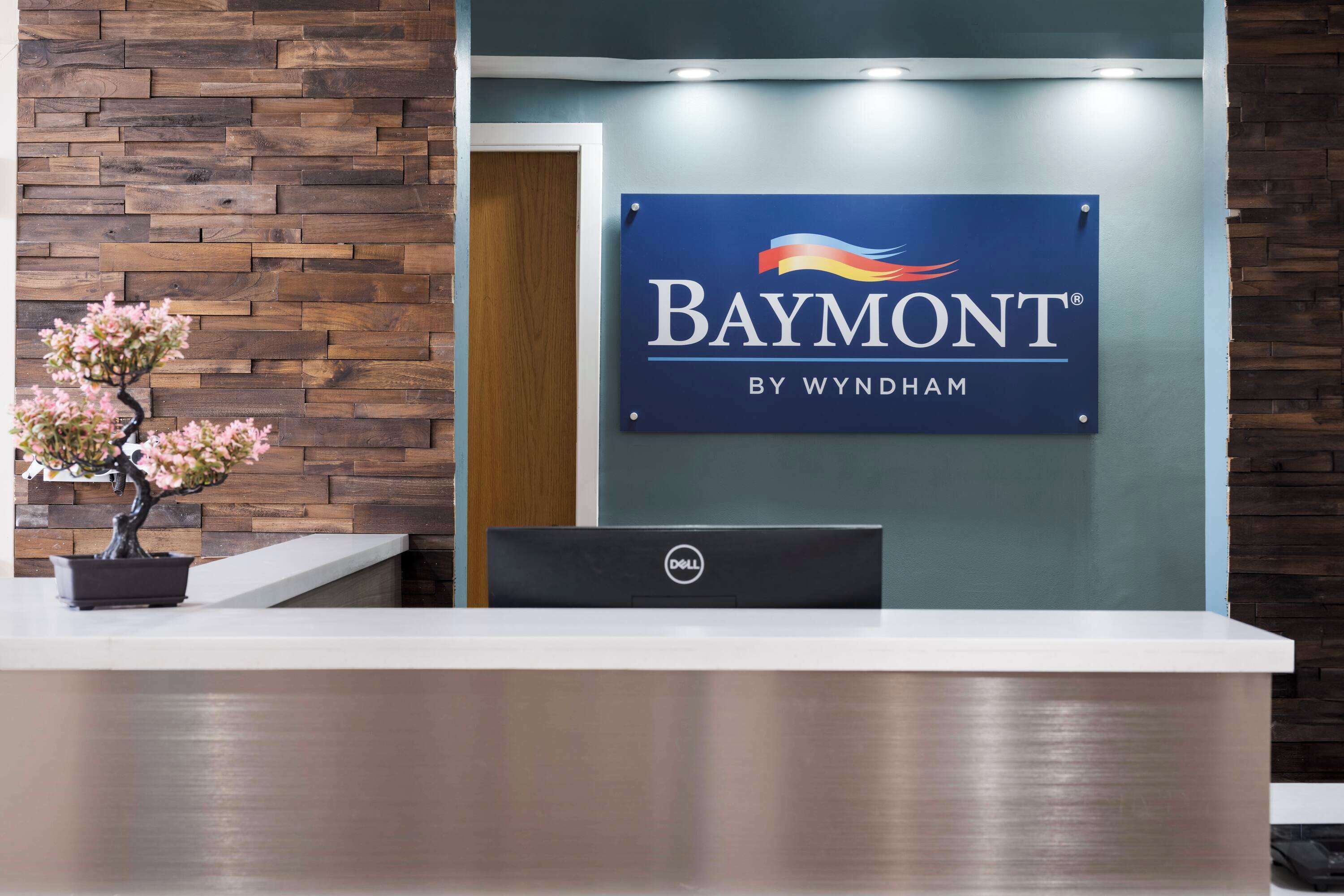 Un mostrador de recepción con un cartel que dice "Baymont by Wyndham" y una computadora Dell.