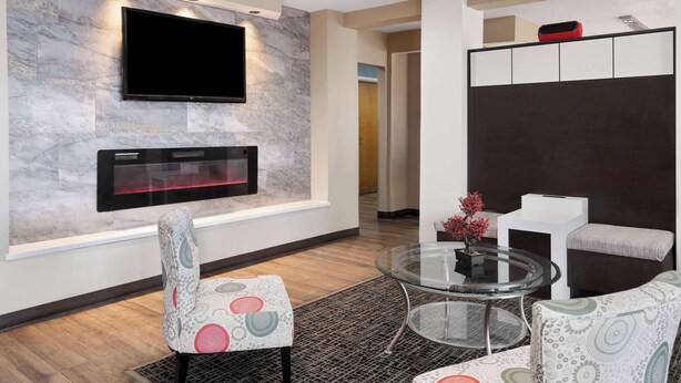 A modern living room with a flat-screen TV mounted on a marble wall, a fireplace below it, and a glass coffee table. - Baymont by Wyndham Boardman (Boardman)