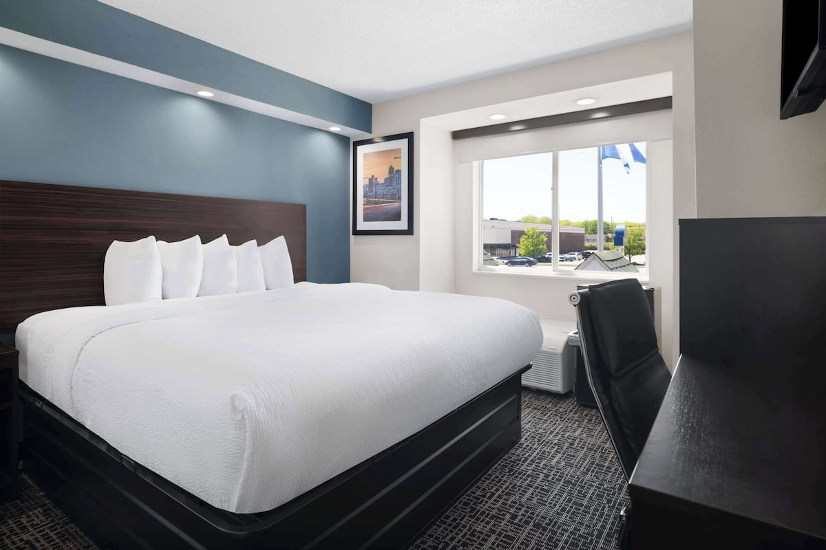 A hotel room with a large bed, a desk, and a window with a view of the outside.