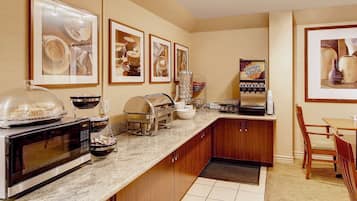 Cocina de hotel con una barra de desayuno buffet, que incluye un microondas, una estación de café y una exhibición de frutas.