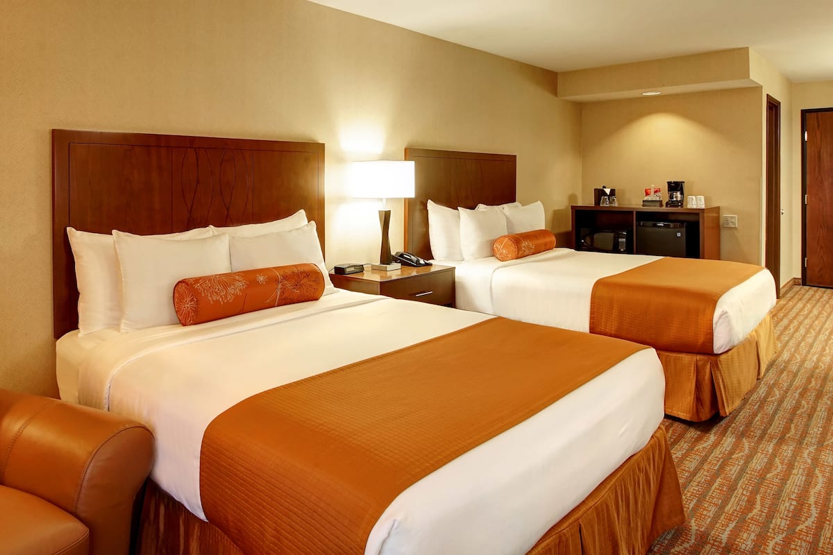 A hotel room with two beds, a desk, a chair, and a lamp.