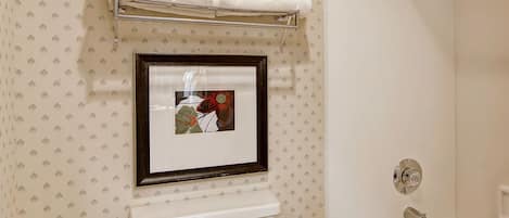 A bathroom with a toilet, a framed picture, a towel rack with towels, and a bathtub.