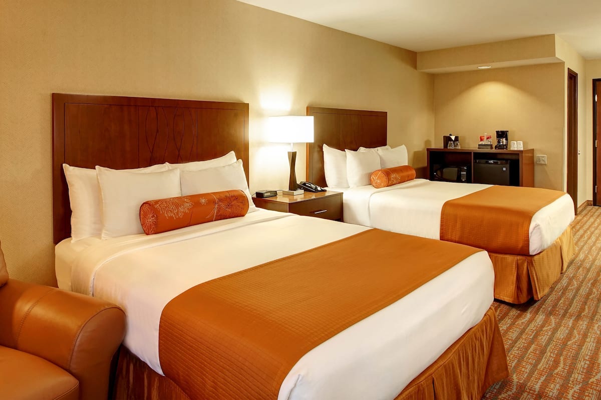 A hotel room with two beds, a desk, a chair, and a lamp.
