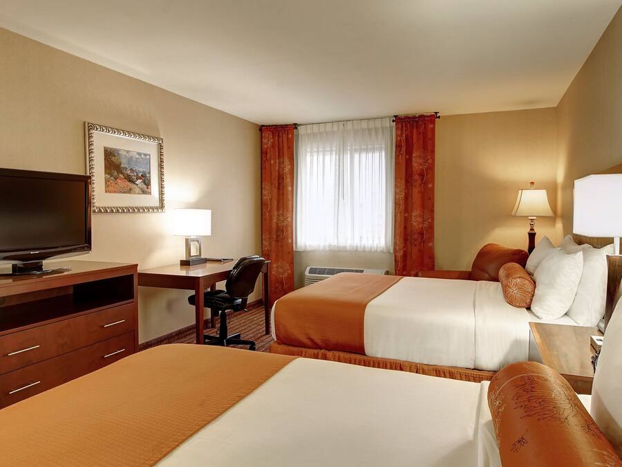 Hotelkamer met twee bedden, een bureau met een televisie, een stoel, een lamp en een raam met gordijnen.