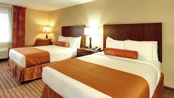 A hotel room with two beds, each with a brown bedspread, white pillows, and a wooden headboard. There is a nightstand with a lamp and a phone between the beds.