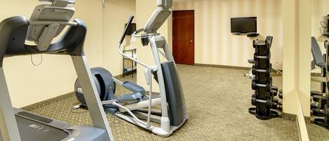 Une salle de sport d’hôtel équipée de tapis de course, d’un appareil elliptique et d’un banc de musculation.