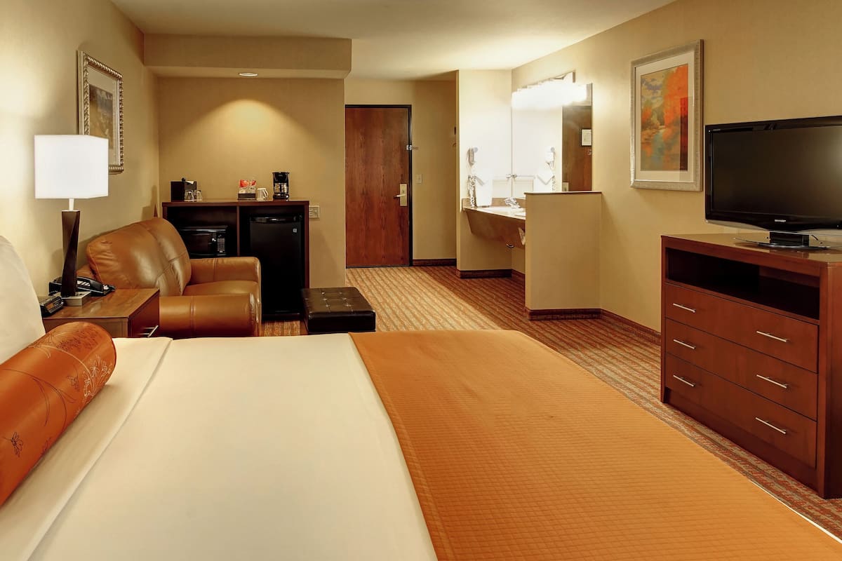 A hotel room with a large bed, a desk with a computer, a television, and a bathroom with a mirror and sink.