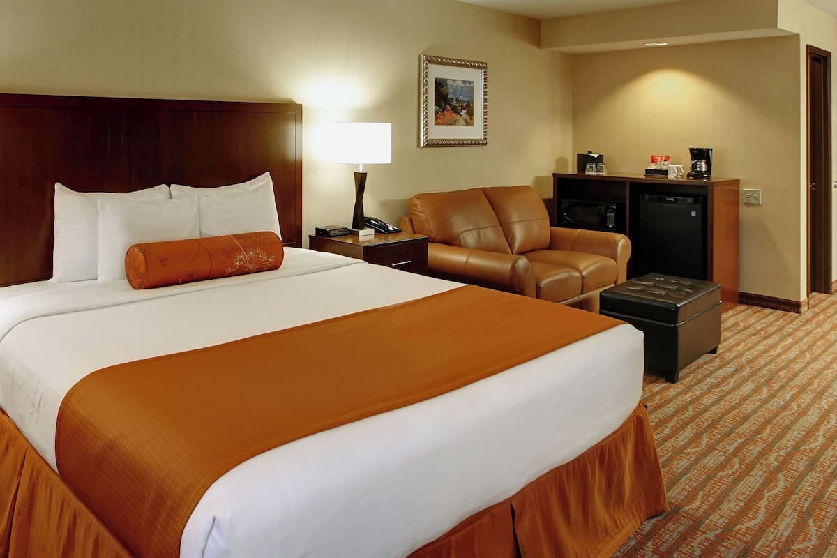 A hotel room with a large bed, two bedside tables, a desk, a leather chair, a coffee maker, and a refrigerator.